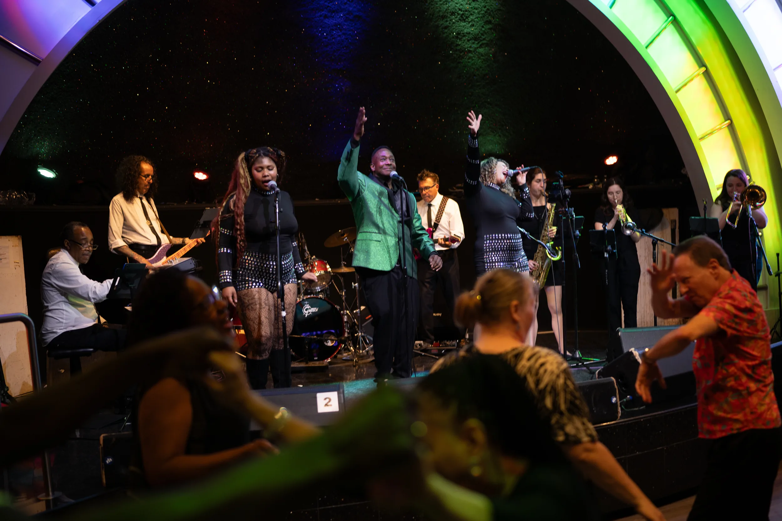 The full band onstage beneath a lit archway as guests dance