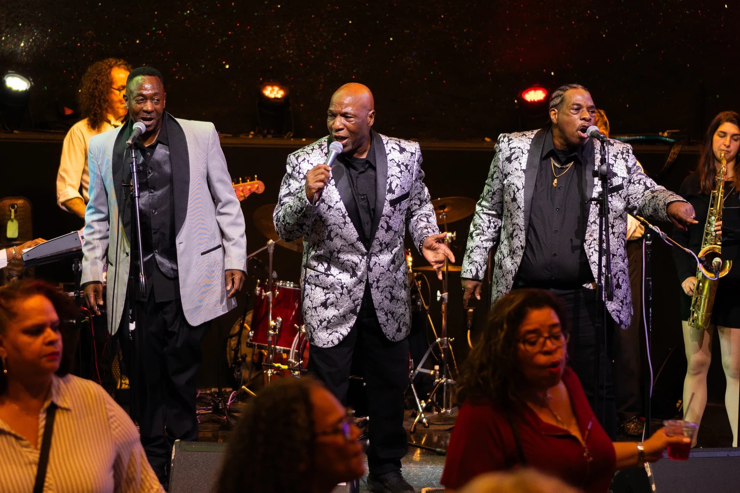 Three vocalists in brocade jackets singing to the crowd