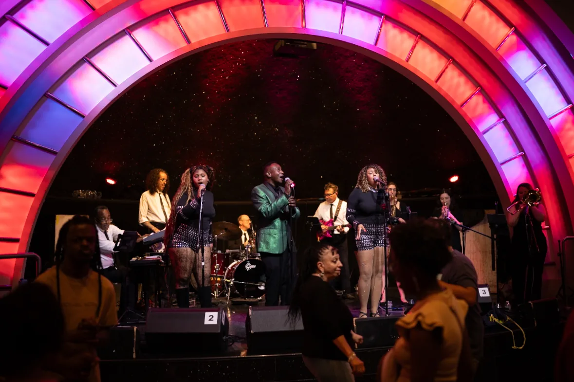 The full band framed by a glowing stage arch
