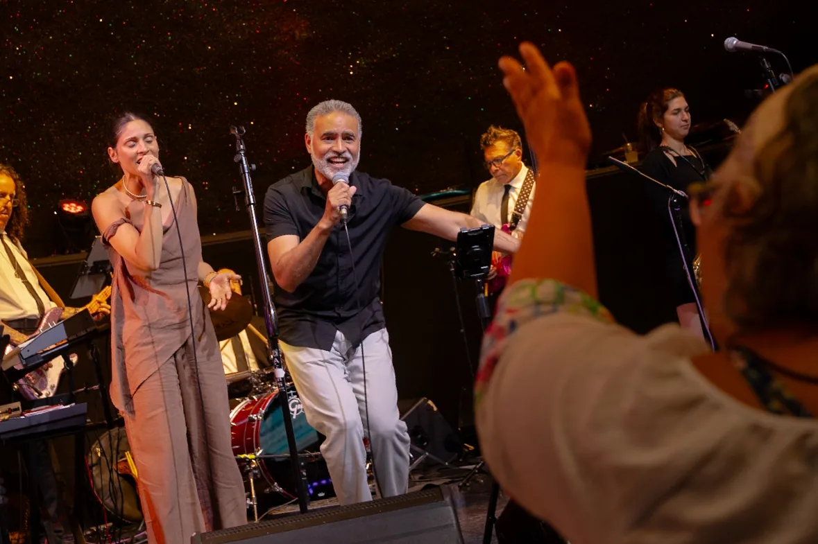 Two vocalists singing at the front of the stage as a guest cheers
